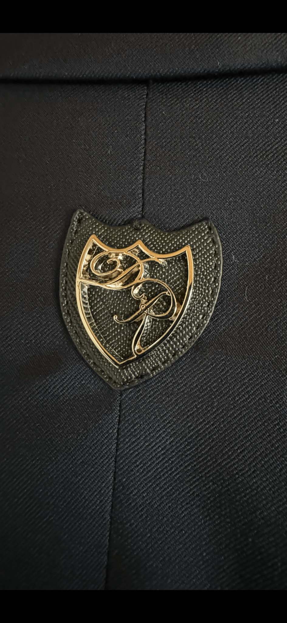 Detailansicht: Dezent platziertes Metalllogo auf der Passe des tiefschwarzen Signature Anzugs.