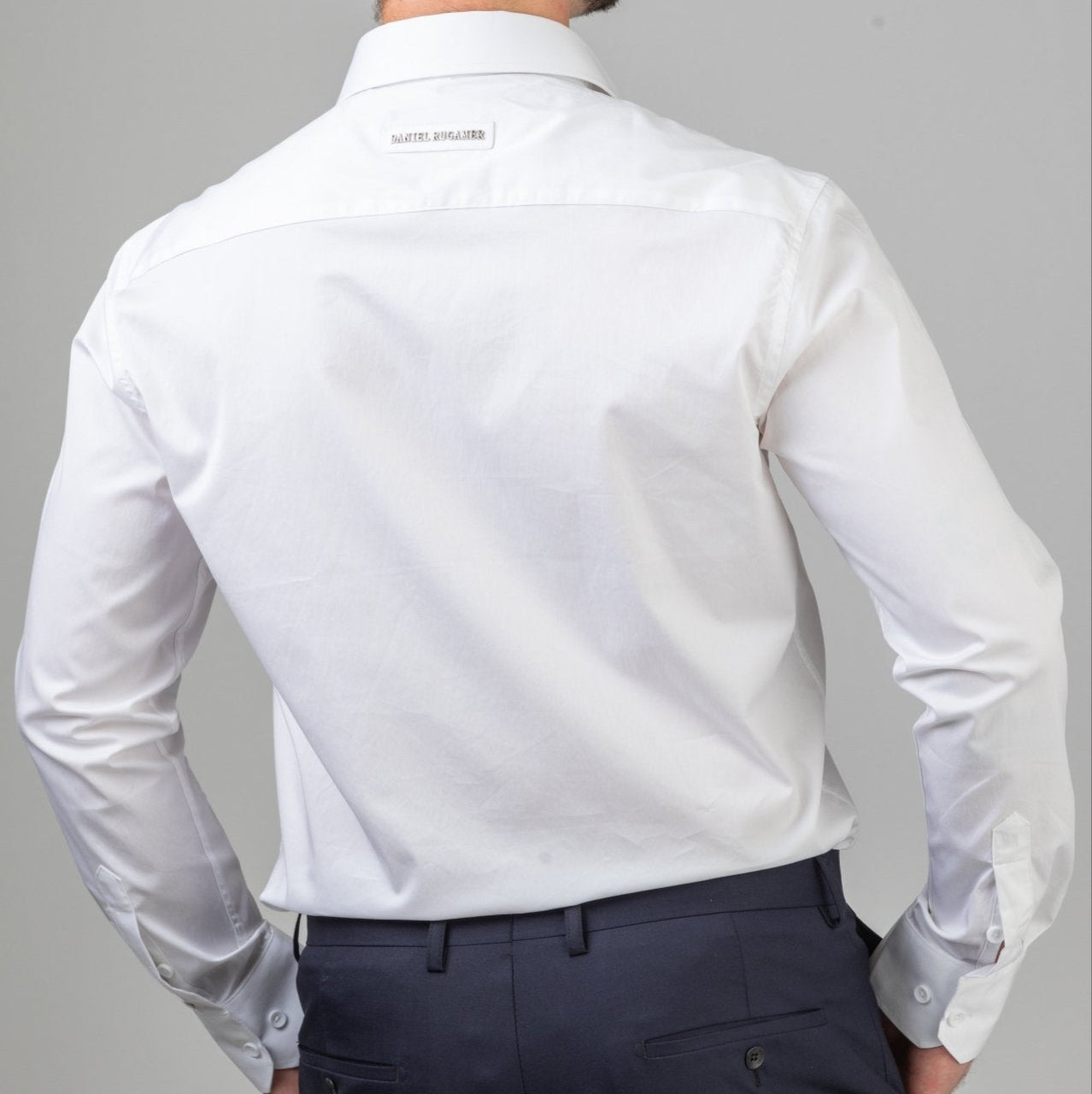 Rückansicht des weißen Signature Hemds - dezenter Metallname auf der Passe, Symbol handwerklicher Perfektion und zeitloser Eleganz passend zur Marineblaue Hose.
