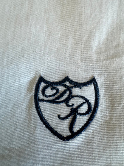 Präzise gesticktes blaues Wappenlogo auf weißem Stoff - Symbol kraftvoller Eleganz und luxuriöser Zurückhaltung.