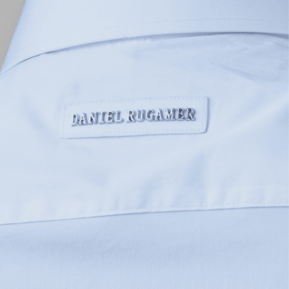 Exklusive Detailaufnahme des Metallnamens Daniel Rügamer am oberen Rücken. Subtiles Luxusmerkmal auf hochwertigem Baumwollgewebe - Understatement mit Wiedererkunngungswert. 