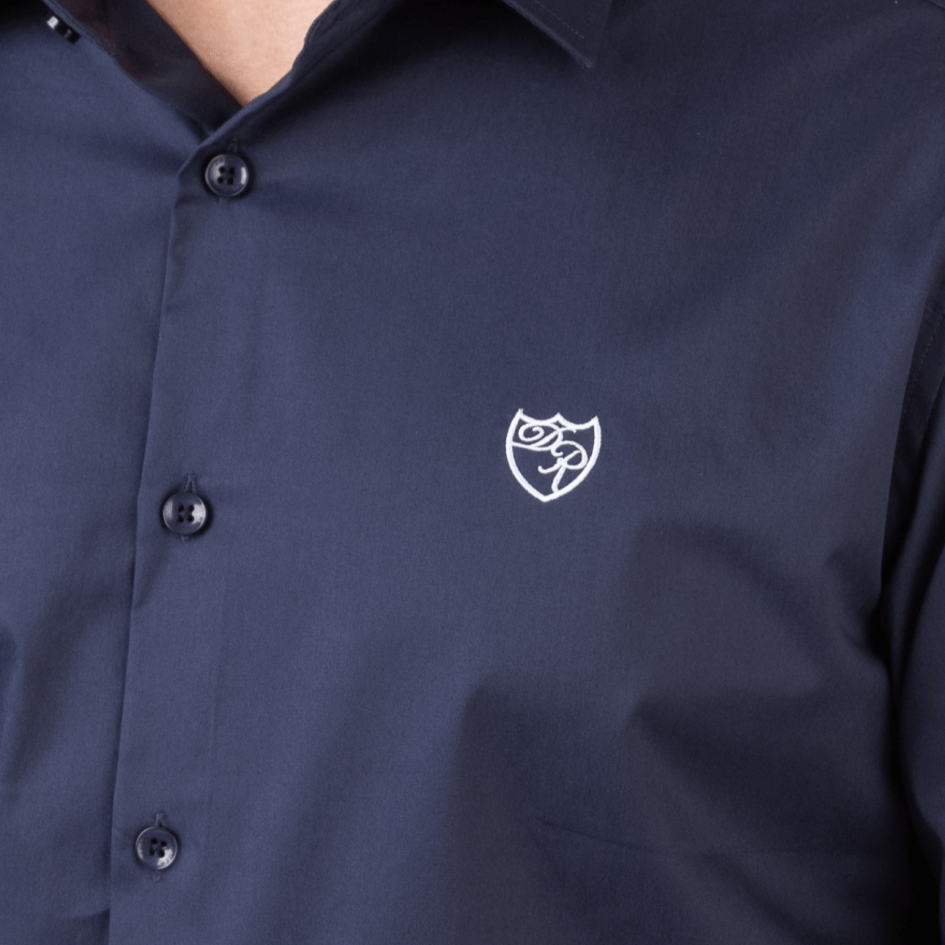 Nahaufnahme der Bruststickerei in Weiß. Feinste Sticktechnik trifft auf tiefes Marineblau - ein elegantes Markenstatement. 