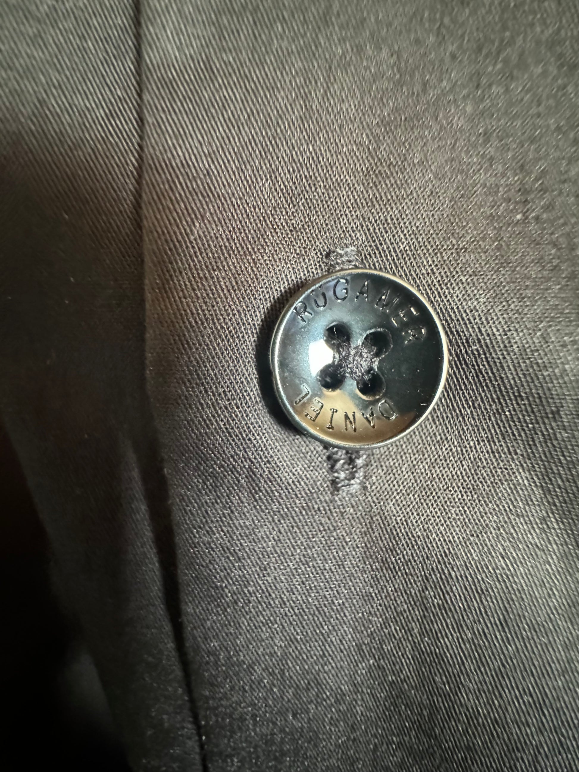 Eleganter schwarzer Knopf mit feiner Struktur - hochwertiges Detail für maskuline Raffinesse.
