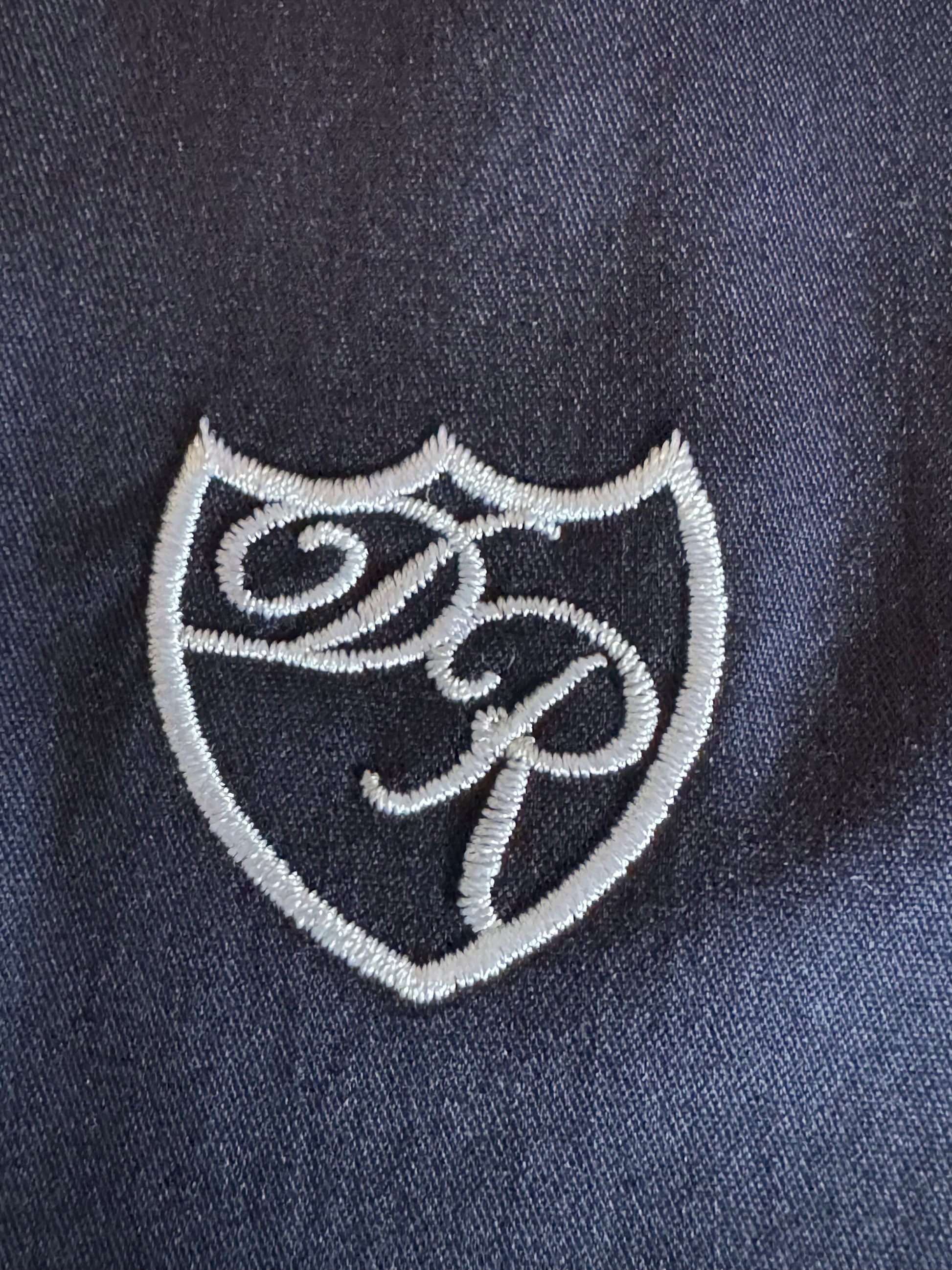 Präzise handgesticktes Wappenlogo in edlem Weiß - exklusives Detail auf luxuriösem Baumwollstoff. 