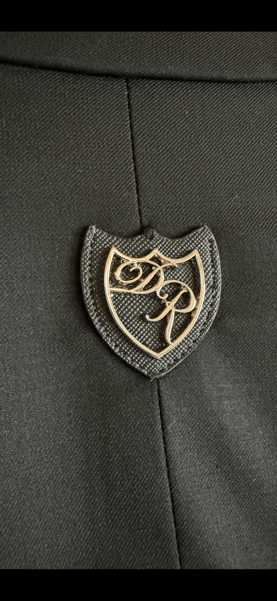 Exklusives Metalllogo Daniel Rügamer - luxuriöse verarbeitet auf der Passe des schwarzen Signature Anzugs.