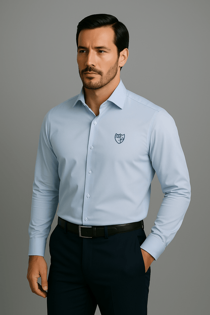 Hellblaues Signature Hemd aus feinster italienischer Baumwolle mit edlem dunkelblauen Wappenlogo - lässige Frontansicht mit Hand-in-der-Tasche-Geste, Ausdruck entspannter Eleganz.
